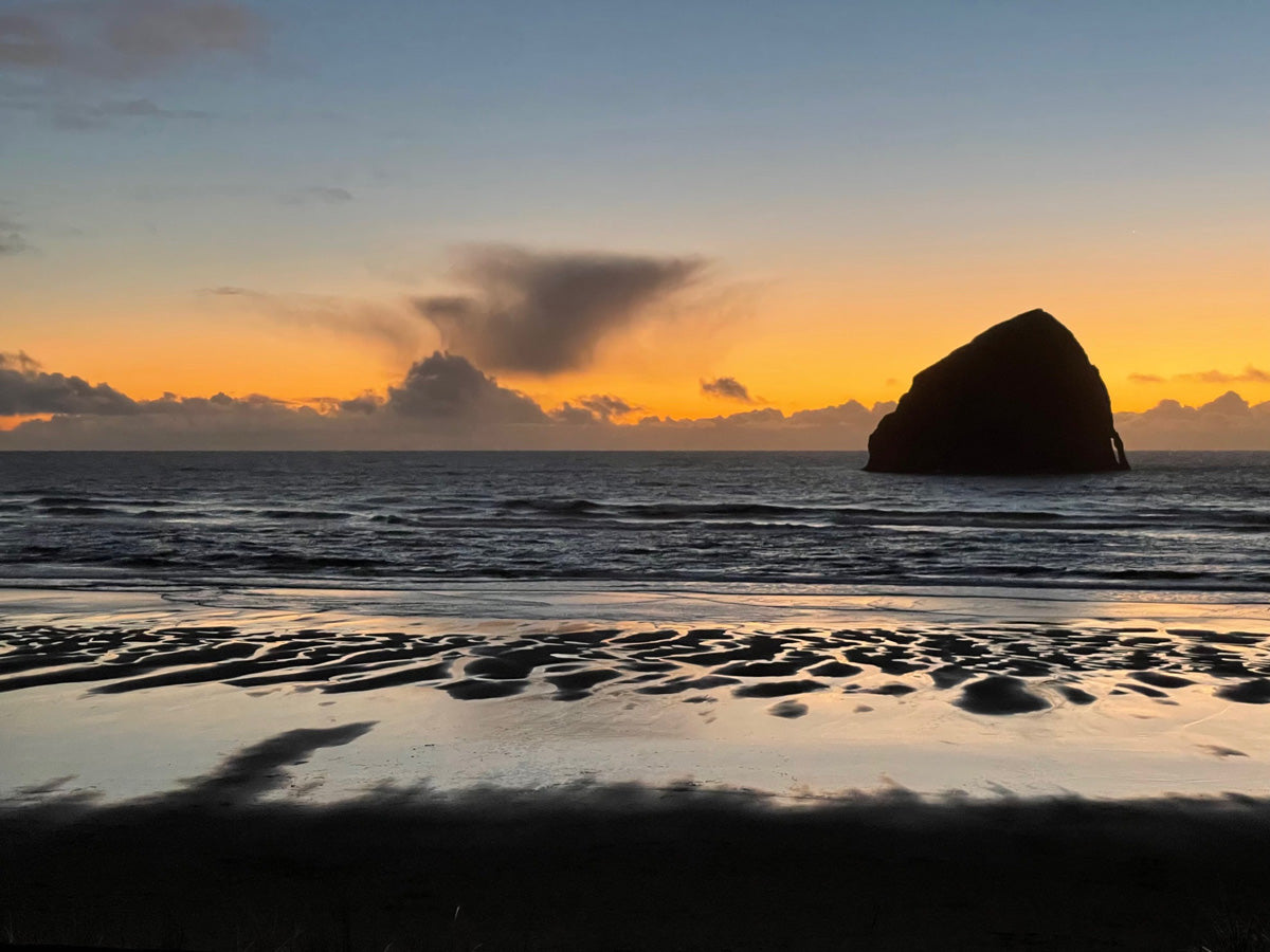 Sunset over the ocean with a large rock formation on a beach