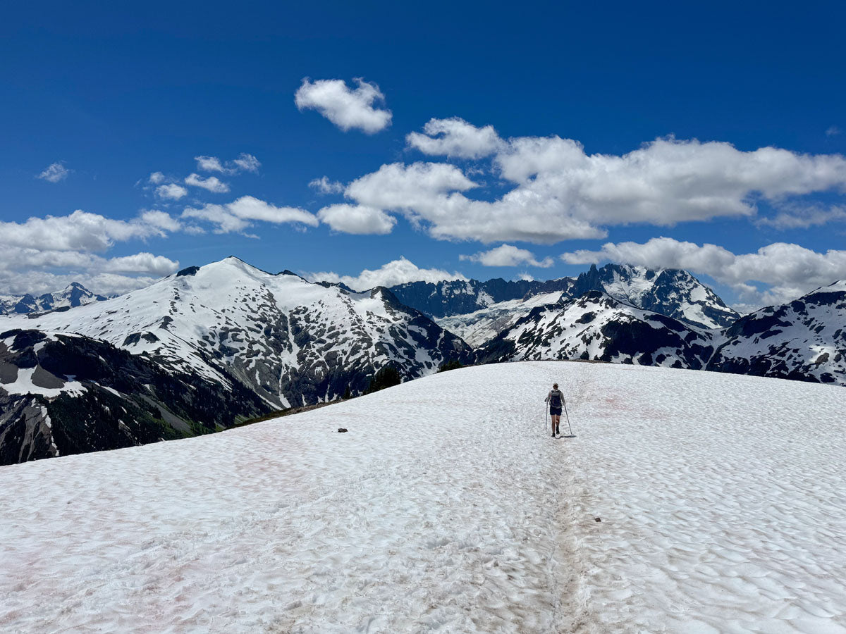 Person standing on a snow-covered mountain with snow-capped peaks and blue sky in the background