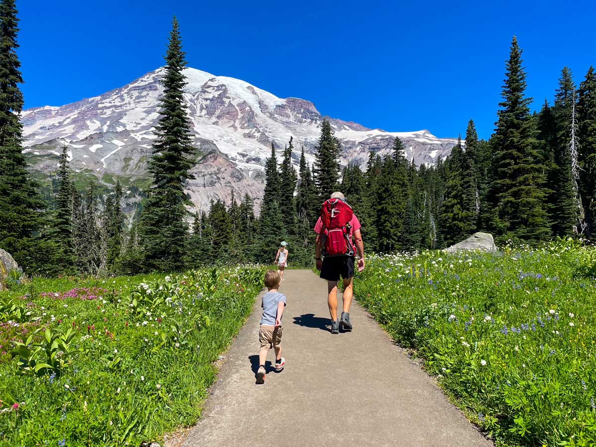 Two hikers walking on a trail with mountains and trees in the background