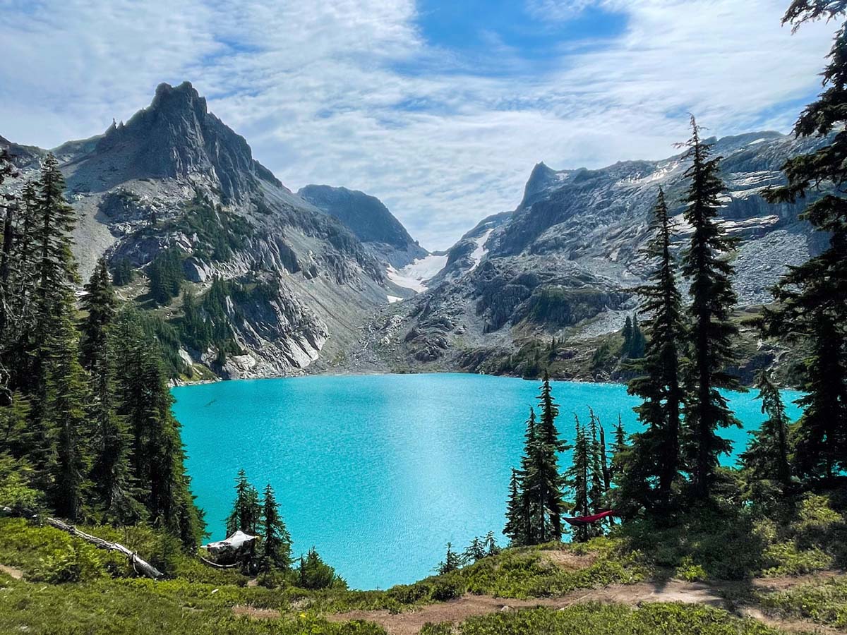 Mountain lake surrounded by trees and rocky mountains under a blue sky.