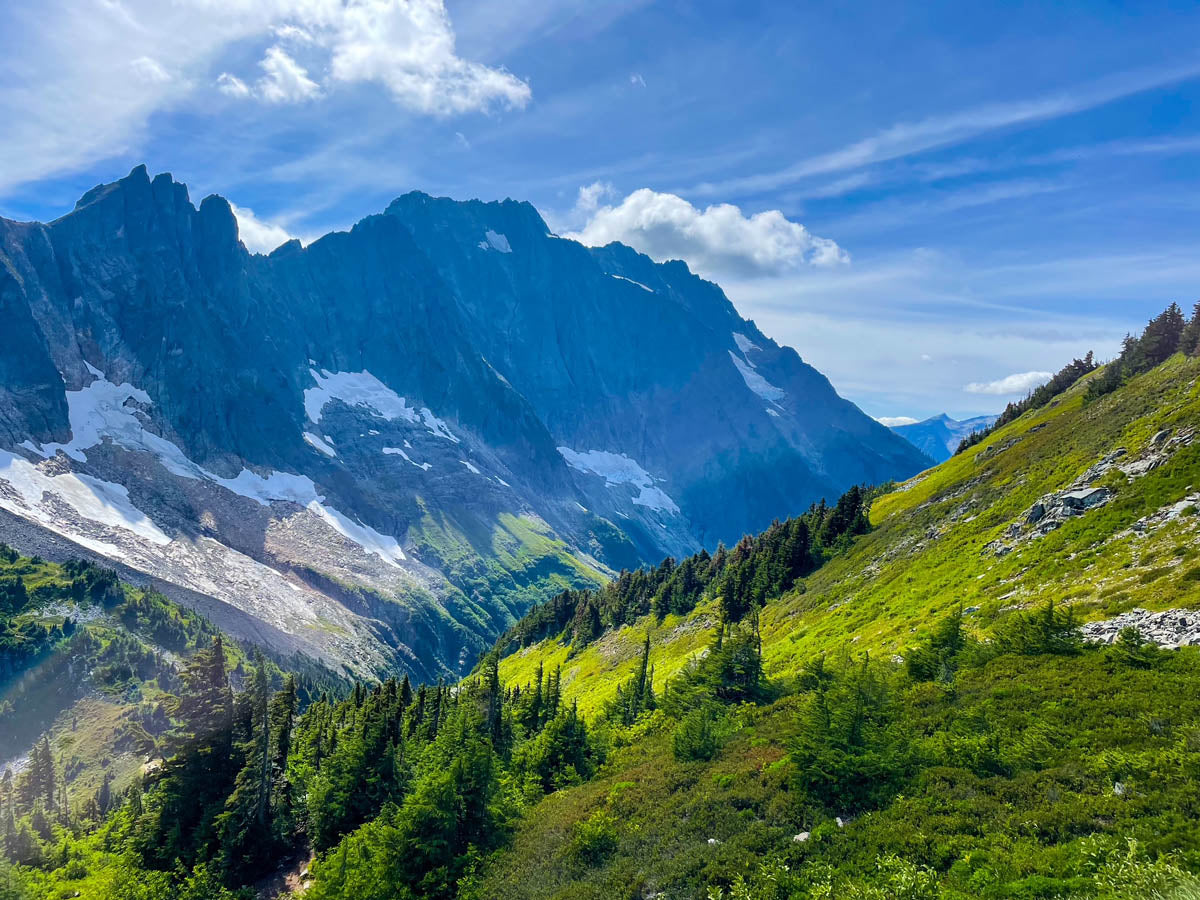 Mountain landscape with green slopes and snow-capped peaks under a blue sky.